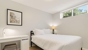 Ein Schlafzimmer mit einem Bett, einem Schreibtisch, einem Stuhl, einer Nachttischlampe und einem Fenster.