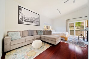 A modern living room with a sectional sofa, a bed, and a large window. - The Garden House & Studio (San Diego)