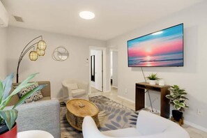 A modern living room with a flat-screen TV, a sofa, a coffee table, and decorative lighting. - The Garden House & Studio (San Diego)