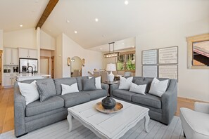 Ein geräumiges Wohnzimmer mit einem grauen Ecksofa, einem weißen Couchtisch und einer Küche im Hintergrund.