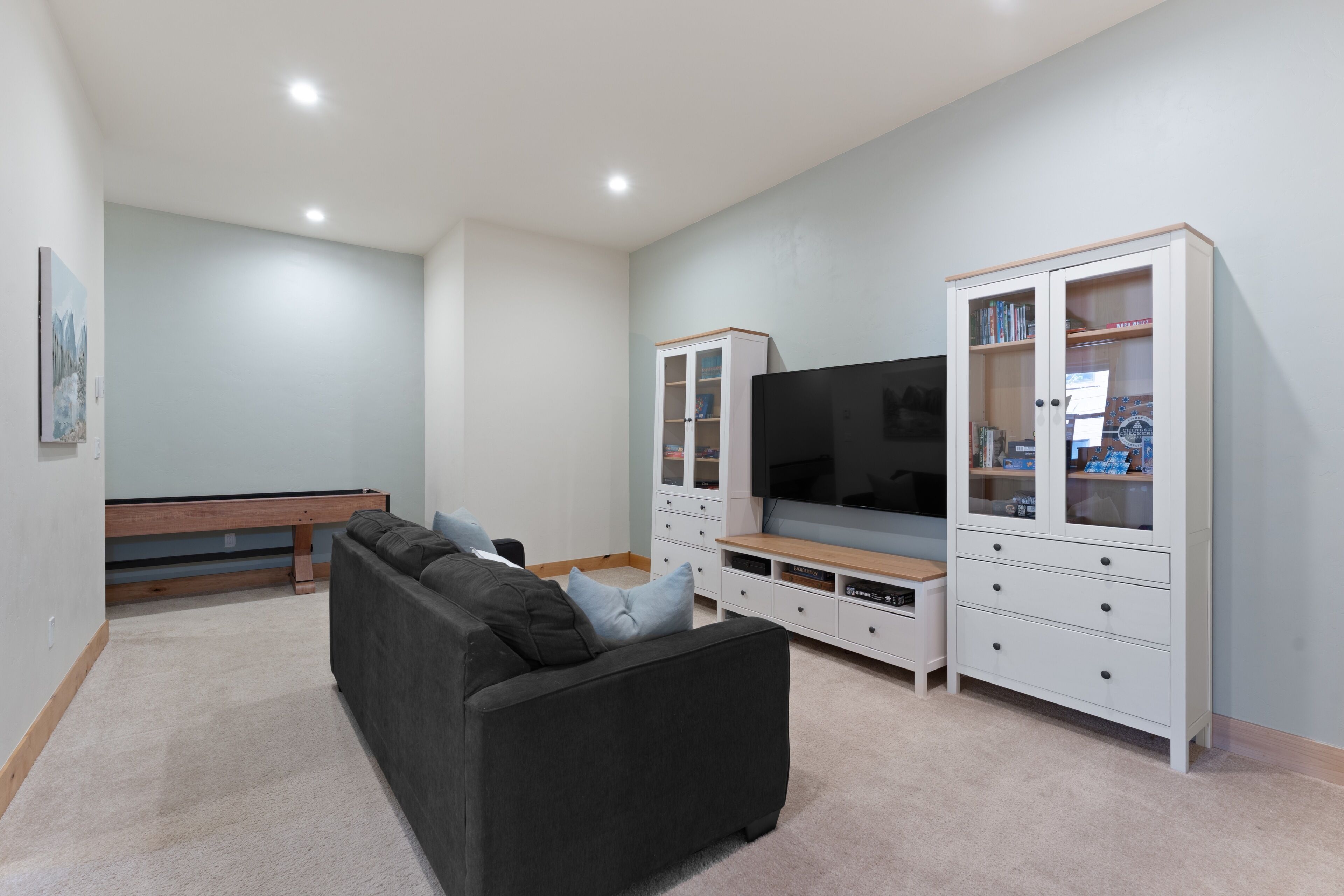 A living room with a black sofa, a flat-screen TV, and white cabinets with glass doors.