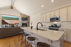 A modern kitchen with a large island, built-in appliances, and a stone fireplace. - Perfect Family Getaway: 4BR with Stunning Alpine Views (Keystone)
