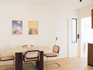 A dining area with a round table, four chairs, and two posters on the wall. - Charming 1-bedroom flat in the 9th (Paris)