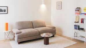 Ein Wohnzimmer mit einem beigen Sofa, einem Couchtisch, einem Bücherregal und einem gerahmten Bild an der Wand.