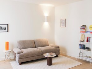Ett vardagsrum med en beige soffa, ett soffbord, en bokhylla och en inramad tavla på väggen.