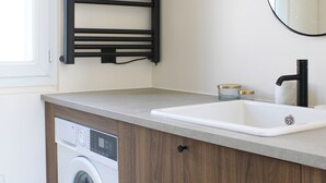 Ein modernes Badezimmer mit integrierter Waschmaschine, einem Waschbecken mit schwarzem Wasserhahn und einem Handtuchhalter.