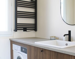 Ett modernt badrum med en inbyggd tvättmaskin, ett handfat med en svart blandare och en handdukshängare.