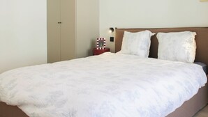 A bed with a white duvet, a brown headboard, and a nightstand with a red and white striped object.