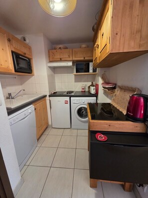 A compact kitchen with a microwave, oven, washing machine, and a coffee maker. - Ski-in/ski-out flat with terrace and pool (Flumet)