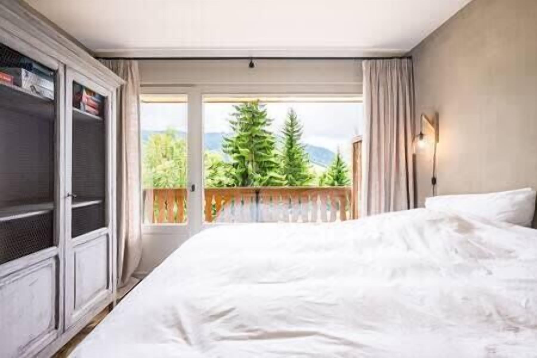 A hotel room with a large bed, a wardrobe, a balcony with a view of trees and mountains.