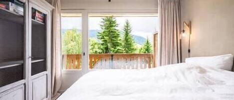A hotel room with a large bed, a wardrobe, a balcony with a view of trees and mountains.