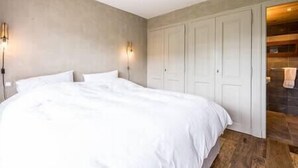 Ein Schlafzimmer mit einem großen Bett, zwei Wandleuchten, einem Kleiderschrank und einem durch eine offene Tür einsehbaren Badezimmer.