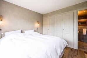Ein Schlafzimmer mit einem großen Bett, zwei Wandleuchten, einem Kleiderschrank und einem durch eine offene Tür einsehbaren Badezimmer.