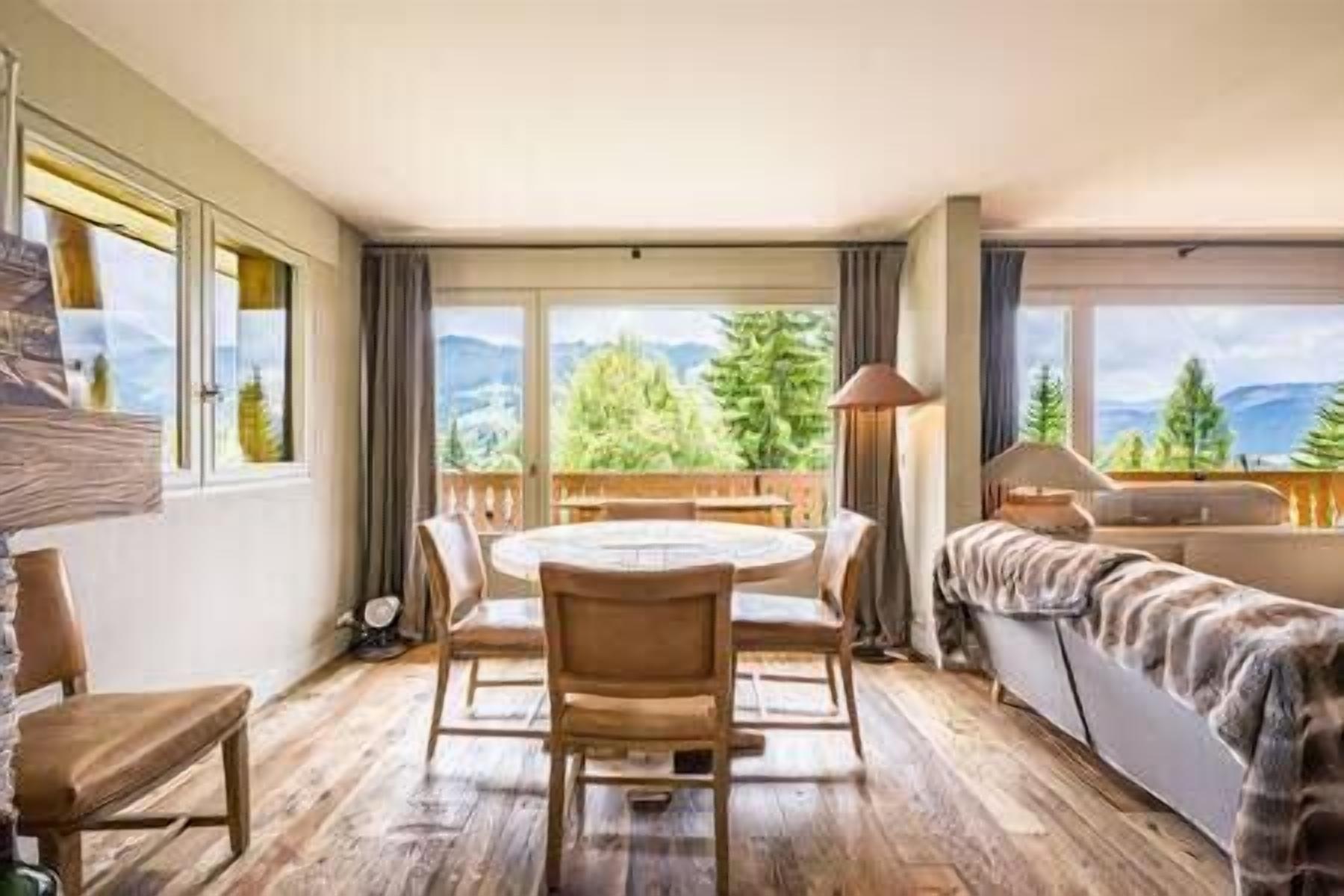 Ein Zimmer mit Holzboden, einem runden Tisch mit Stühlen, einer Couch und Bergblick durch große Fenster.