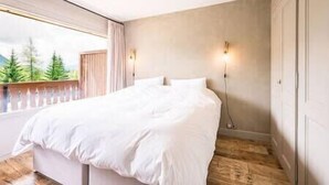 Ein Schlafzimmer mit einem großen Bett, einem Fenster mit Blick auf Bäume und einer Wandleuchte.