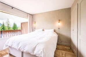 Ein Schlafzimmer mit einem großen Bett, einem Fenster mit Blick auf Bäume und einer Wandleuchte.