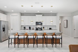 A modern kitchen with white cabinets, a central island with bar stools, a stainless steel refrigerator, and a microwave. - 9024 Solara brand new theme rooms pool near club (Kissimmee)