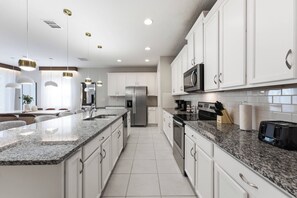 A modern kitchen with white cabinetry, granite countertops, stainless steel appliances, and pendant lighting. - 9024 Solara brand new theme rooms pool near club (Kissimmee)