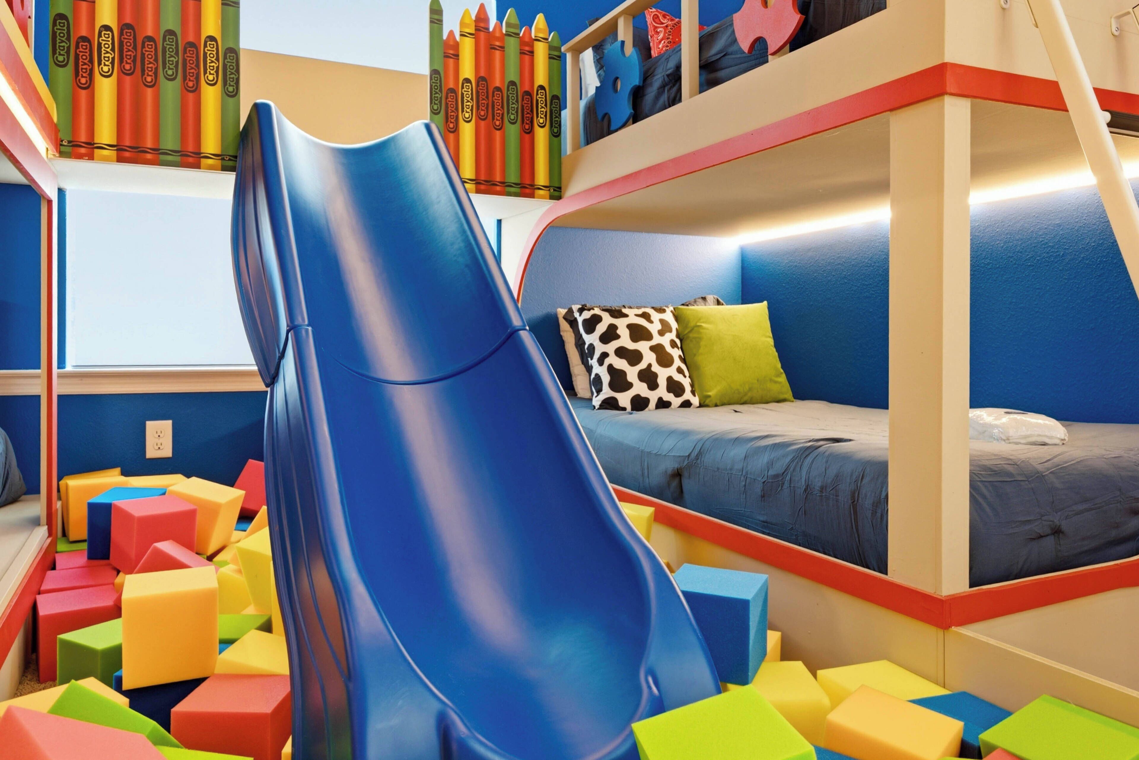 A children's play area with a blue slide, colorful foam blocks, and a bunk bed with a blue mattress.