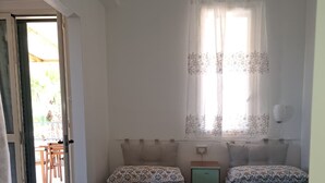 A room with two beds, a small bedside table, a window with curtains, and a door leading to an outdoor area. - The Residences 6 (Marina di Modica)