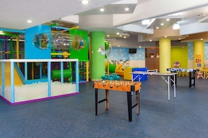 Espaço infantil com estrutura de escalada, piscina de bolinhas e mesa de futebol de mesa.