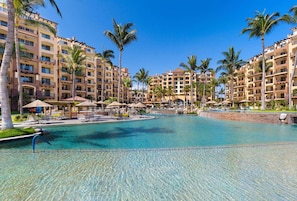 Resort com uma piscina grande, palmeiras e várias varandas.