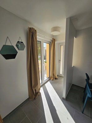 Un couloir avec une porte-fenêtre coulissante donnant sur un balcon, une chaise bleue et deux miroirs fixés au mur.