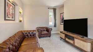 Ein Wohnzimmer mit einem braunen Ledersofa, einem braunen Sessel, einem Fernseher auf einem Holzständer und einem Fenster mit Vorhängen.