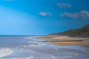 A coastal beach with a wooden jetty extending into the sea, a sandy shore, and a cliff in the background. - Detached Coastal Home - Walk to Beach - Sleeps 4 (Overstrand)