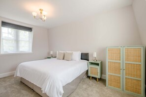 A bedroom with a large bed, two bedside tables, a nightstand, a wardrobe, and a window with blinds. - Detached Coastal Home - Walk to Beach - Sleeps 4 (Overstrand)