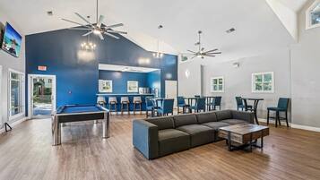 A spacious indoor area with a pool table, a sectional sofa, and multiple ceiling fans.