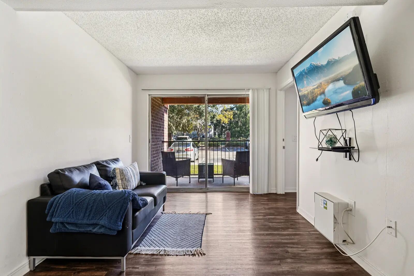 Sala de estar con sofá negro, televisor montado en la pared y vistas al exterior a través de un ventanal.