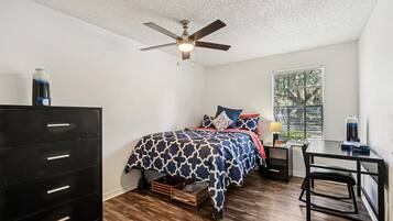 A bedroom with a bed, dresser, desk, and window.
