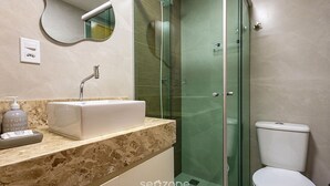Een moderne badkamer met een douchecabine van glas, een wit toilet en een marmeren aanrechtblad met een zeepdispenser.