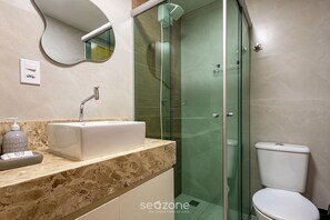 Ein modernes Badezimmer mit einer gläsernen Duschkabine, einer weißen Toilette und einer Marmorplatte mit Seifenspender.