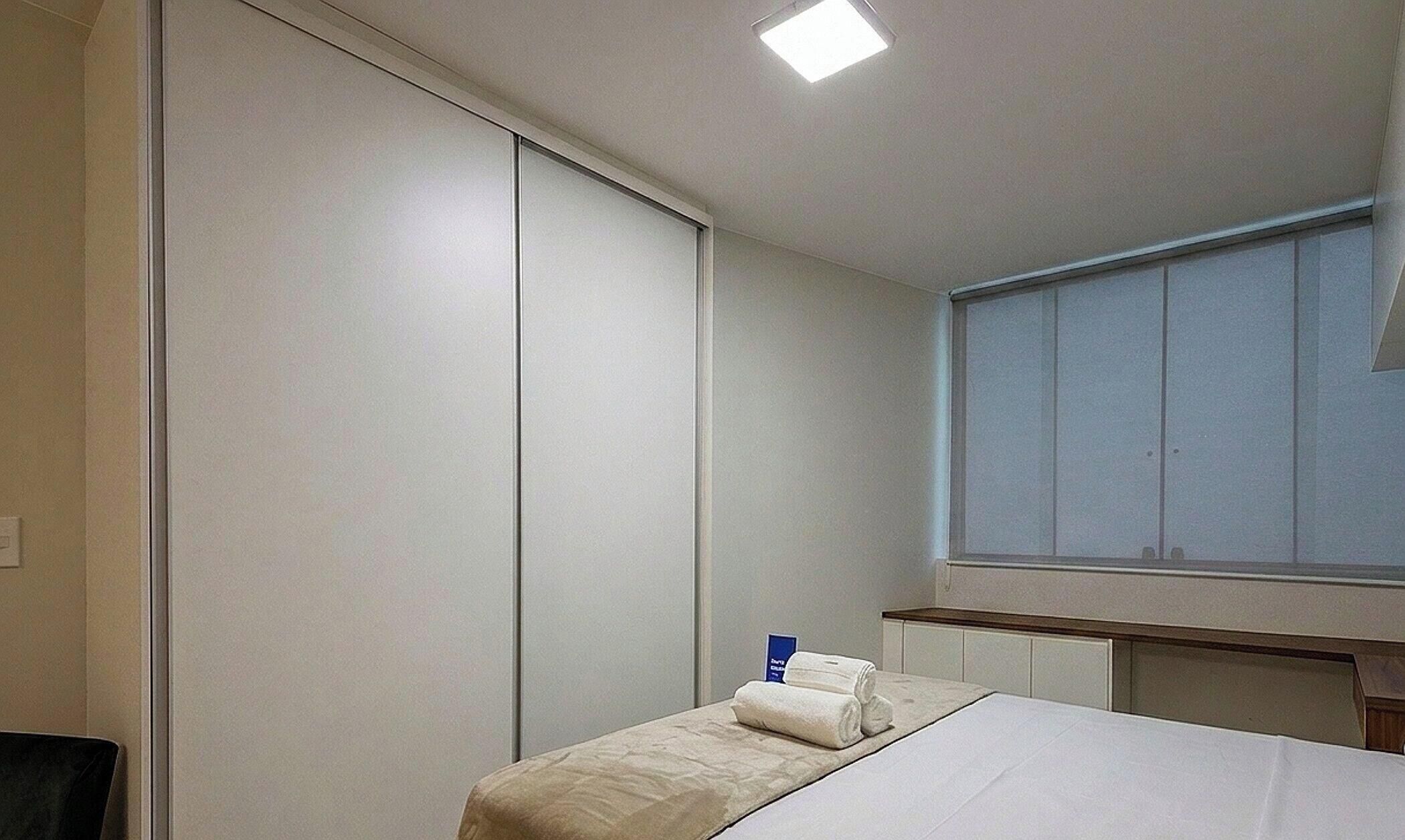 Quarto de hotel com uma cama, mesa de cabeceira, janela e armário.
