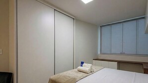 Een hotelkamer met een bed, nachtkastje, raam en kast.