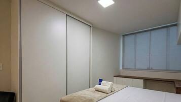 Quarto de hotel com uma cama, mesa de cabeceira, janela e armário.