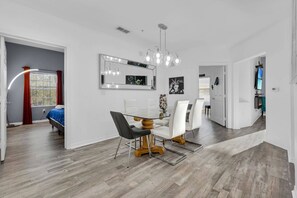 A modern dining area with a glass-top table, white chairs, and a chandelier. - Premium Disney Retreat | Fireplace & Balcony -9051 (Kissimmee)
