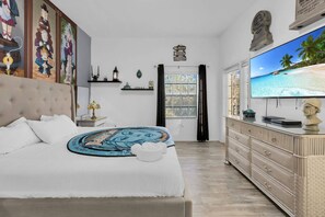 Ein Schlafzimmer mit einem Bett, einem Fernseher, einer Kommode und einem Fenster mit Blick auf den Strand.