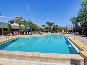 Ein Swimmingpool mit Liegestühlen und Palmen, umgeben von einem Gebäude mit grüner Dachbegrünung.