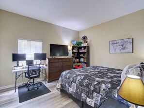 Ein Schlafzimmer mit Schreibtisch, Computer, Fernseher, Bücherregal, Bett und einer Wand mit einem motivierenden Zitat.