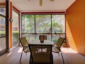A balcony with a table and chairs, a potted plant, and a view of trees and buildings. - Caribe Cove Retreat | Balcony | 2 BD | Near Disney (Kissimmee)