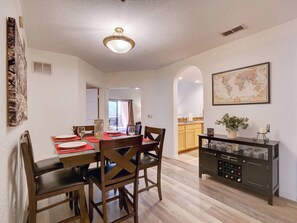 A dining area with a table set for four, wooden chairs, and a cabinet with wine glasses. - Caribe Cove Retreat | Balcony | 2 BD | Near Disney (Kissimmee)