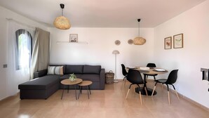 Ein modernes Wohnzimmer mit einer Eckcouch, einem Esstisch mit Stühlen und Pendelleuchten.