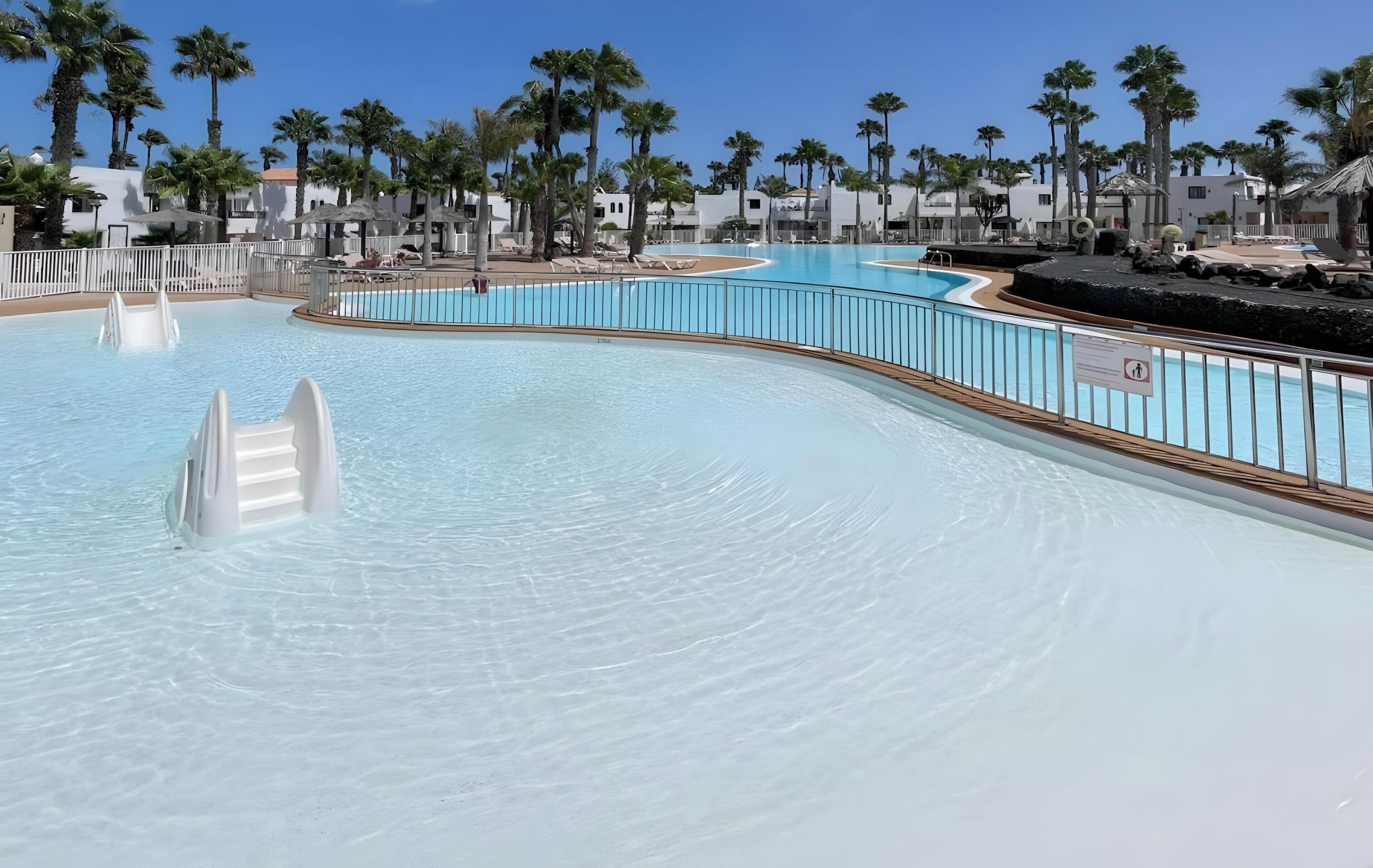 Una piscina con tobogán, rodeada de palmeras y edificios blancos.