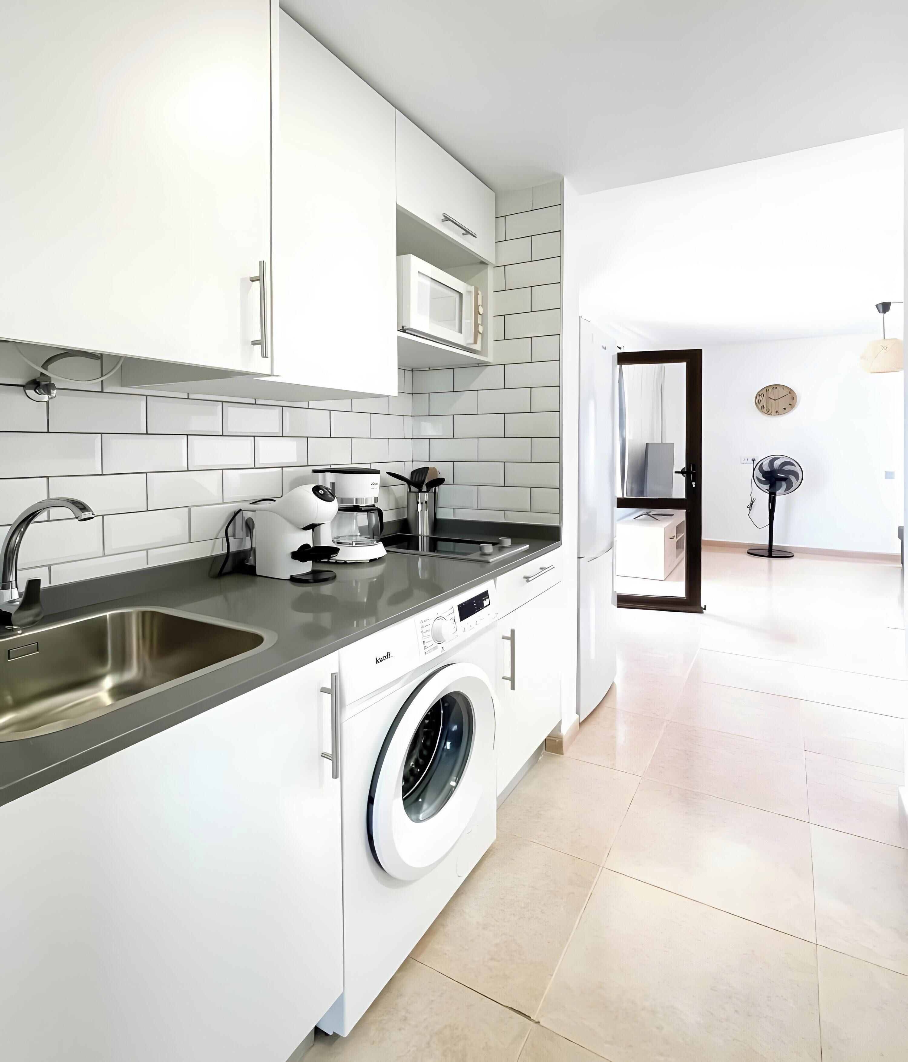 Una cocina moderna con muebles blancos, lavadora integrada y cafetera.