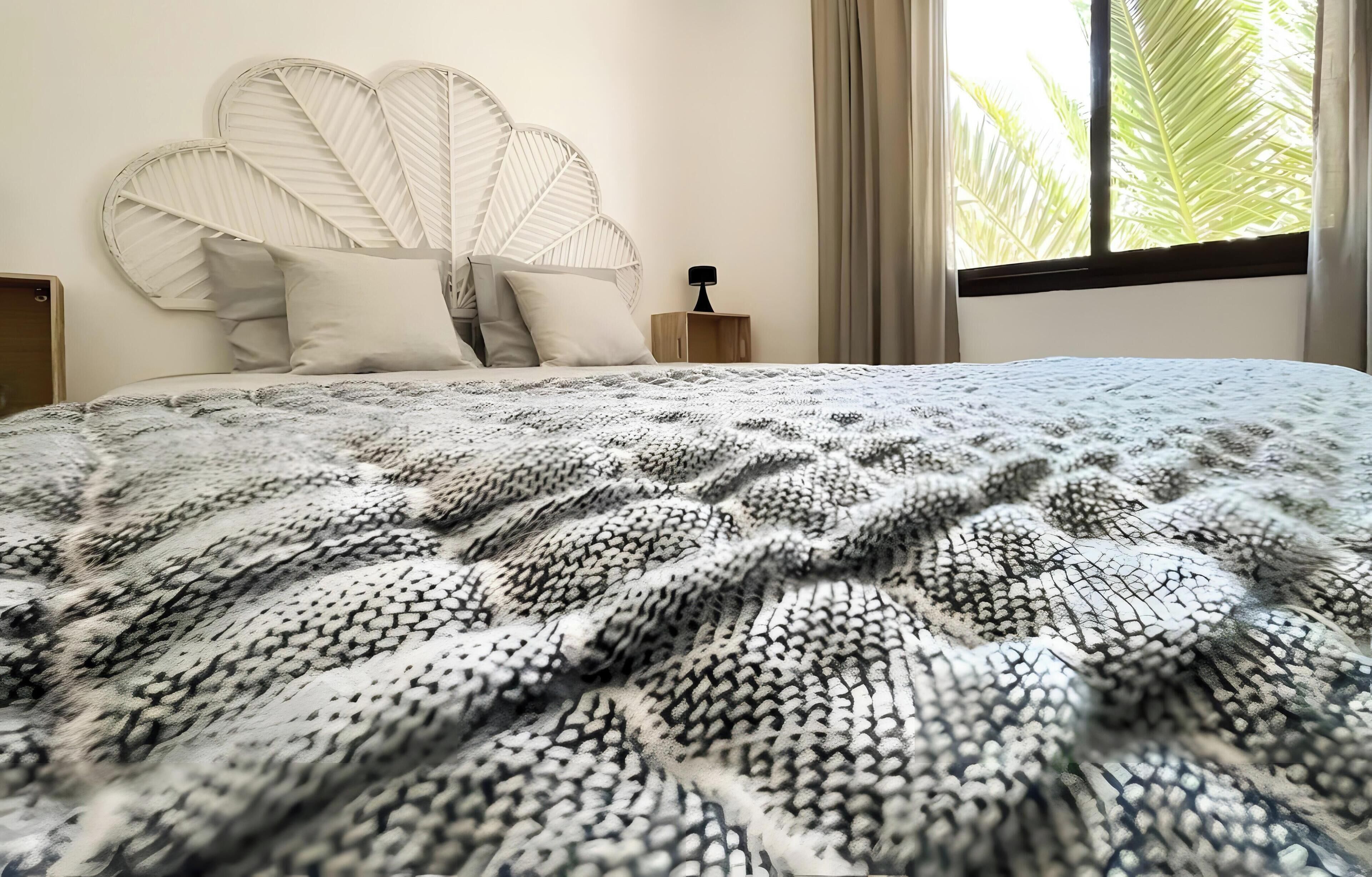 Una cama con una manta estampada, un cabecero blanco y una mesita de noche con una lámpara.