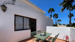 Eine Terrasse mit Tisch und Stühlen, ein Fenster und eine weiße Wand mit dem Palmen-Logo.