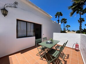 Eine Terrasse mit Tisch und Stühlen, ein Fenster und eine weiße Wand mit dem Palmen-Logo.
